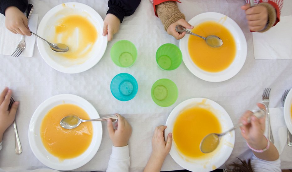 Menores comen un plato de puré en un comedor escolar.